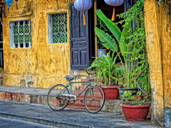 a single bike laying against a yellow building in vietnam