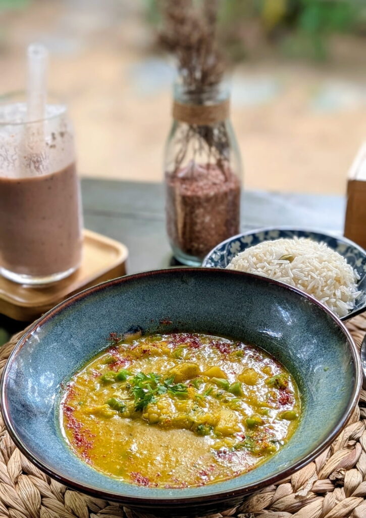 a blue bowl filled with a comforting vegan yellow curry next to a chocolate smoothie at plant lab in hoi an