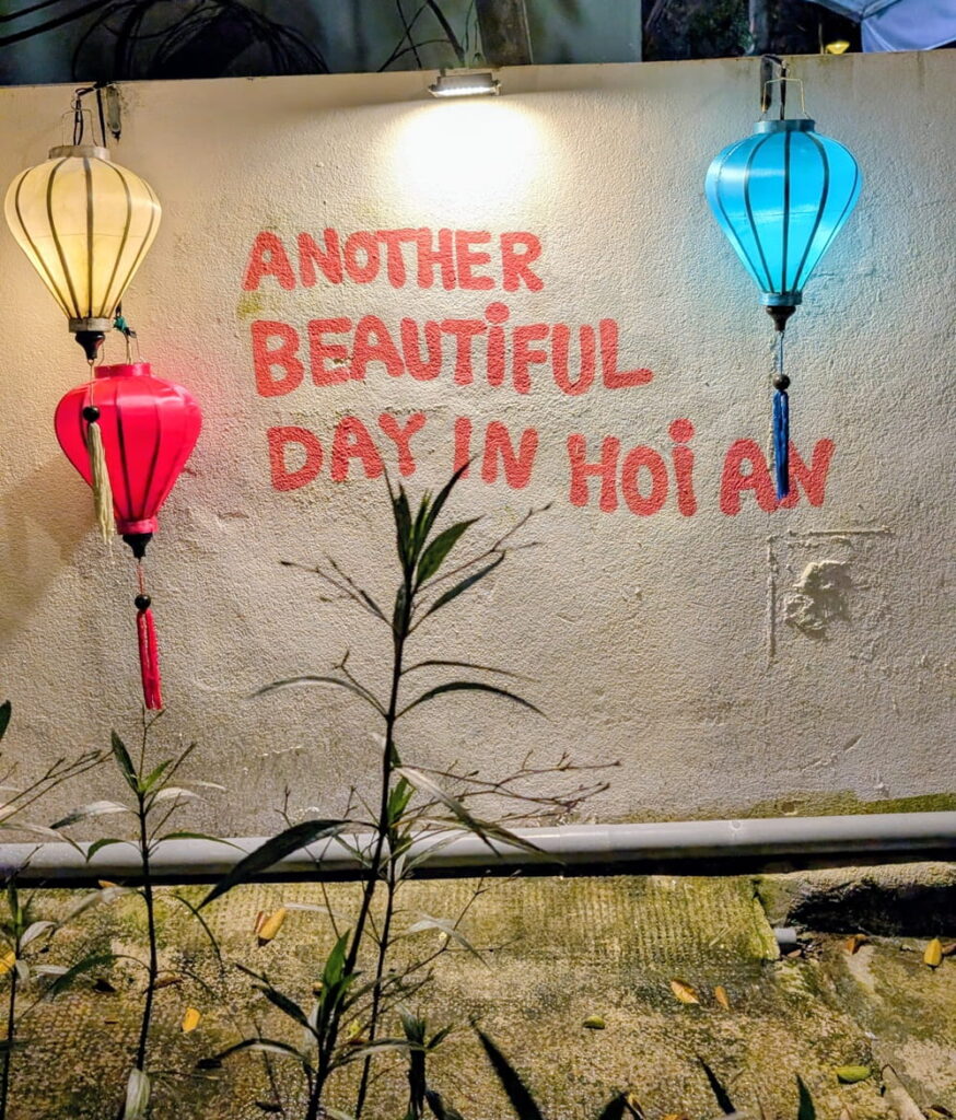 a pink sign on a white wall that says another beautiful day in hoi an