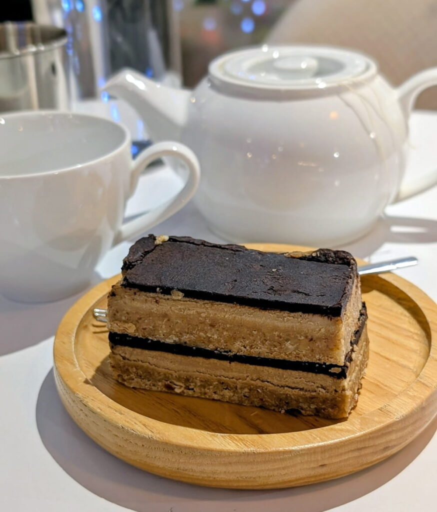 a small sliced of layered chocolate vegan cake next to a white tea pot at kurumi i n hoi an