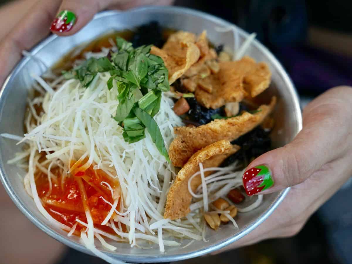 a bowl of vegan noodles with spicy red hot sauce and crispy wonton strips in ho chi mihn vietnam