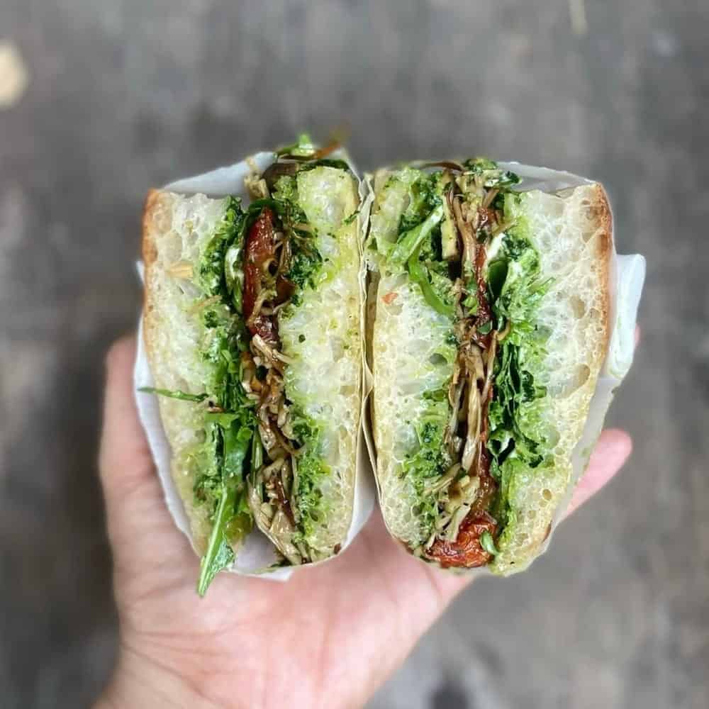 a large vegan sandwich cut into two filled with a bright green pesto and layers of mock meats at La Studio in hanoi