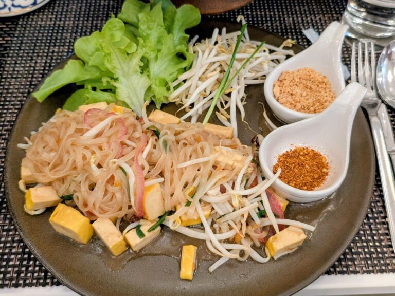 a large black plate with vegan pad thai with chunks of tofu next to small bowls of chili and peanuts in thailand