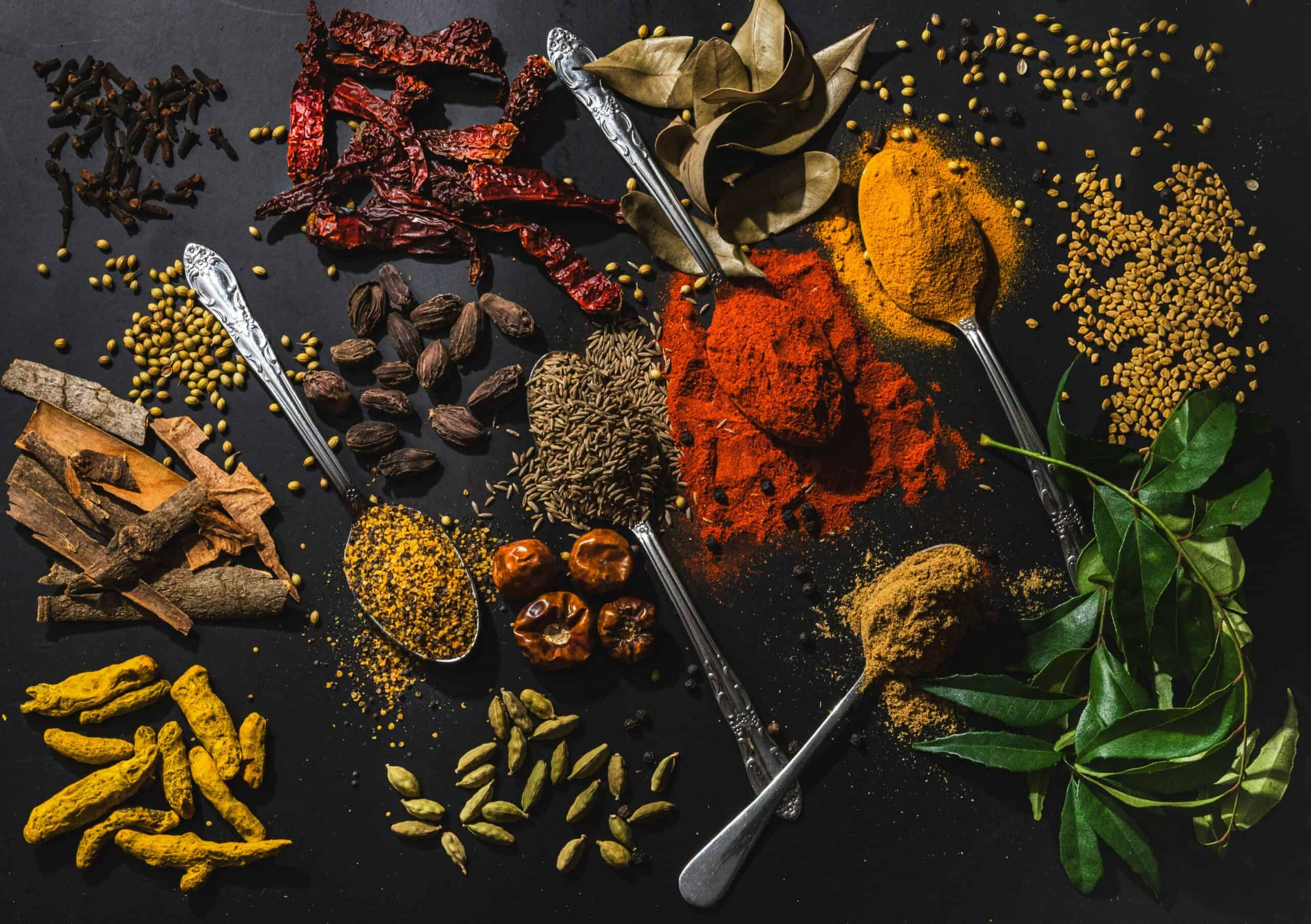 Variety of Indian spices and herbs used in vegan Indian cooking including turmeric, cumin, chili, and cardamom