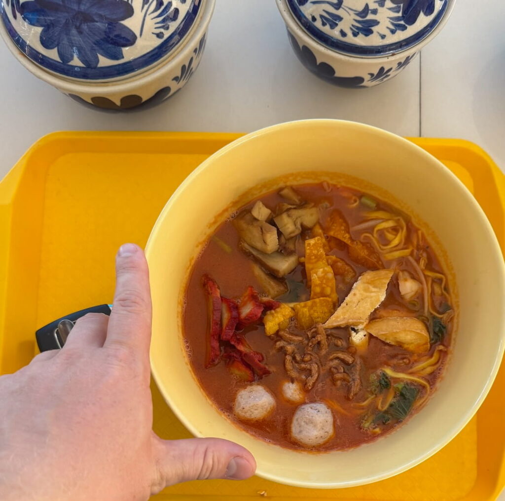 bowl of vegan thai soup with mushroom meatballs and noodles on a yellow tray in thailand