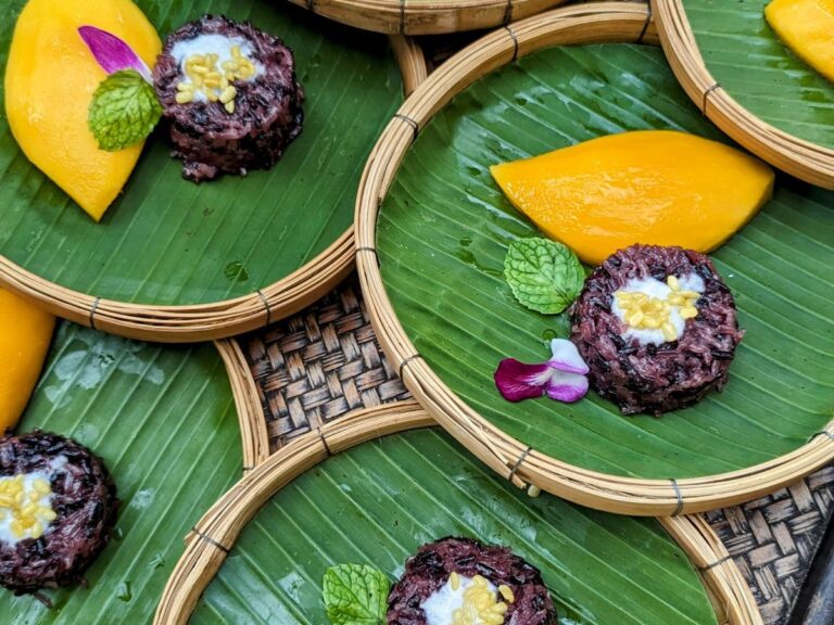 green banana leaf lined plates with chunks of bright yellow mango and purple sticky rice in thailand