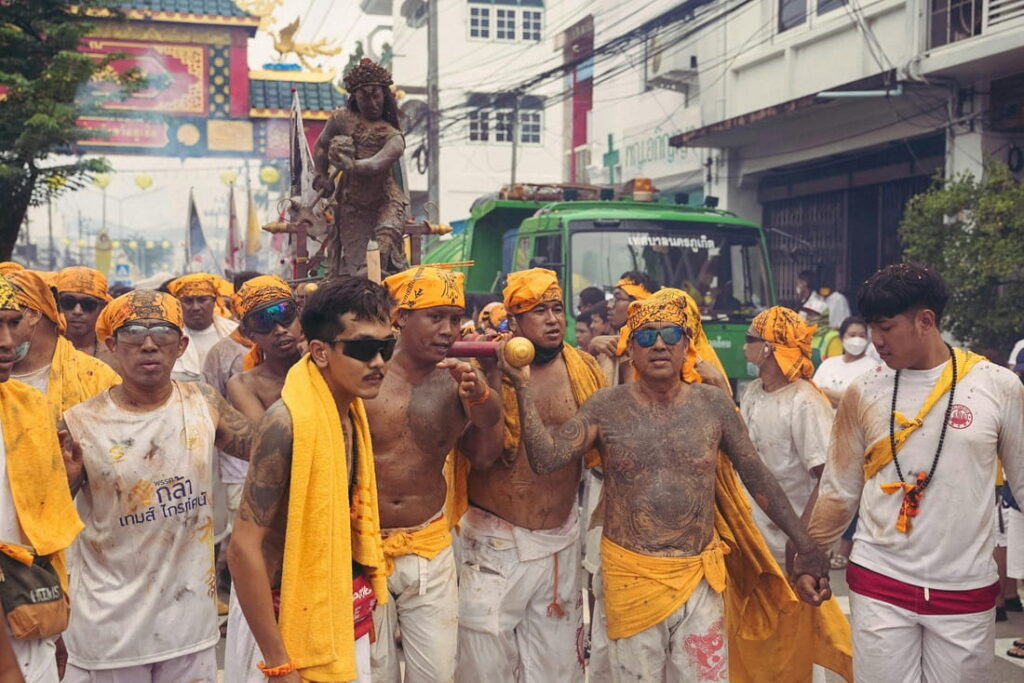 men wearing yellow and white parading down a crowded street in thailand during the vegan festival