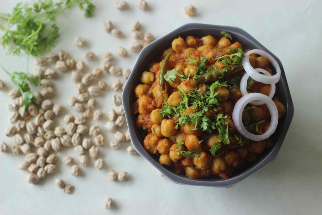 Bowl of authentic chana masala made with chickpeas simmered in a spiced tomato and onion curry, garnished with fresh cilantro and red onion.