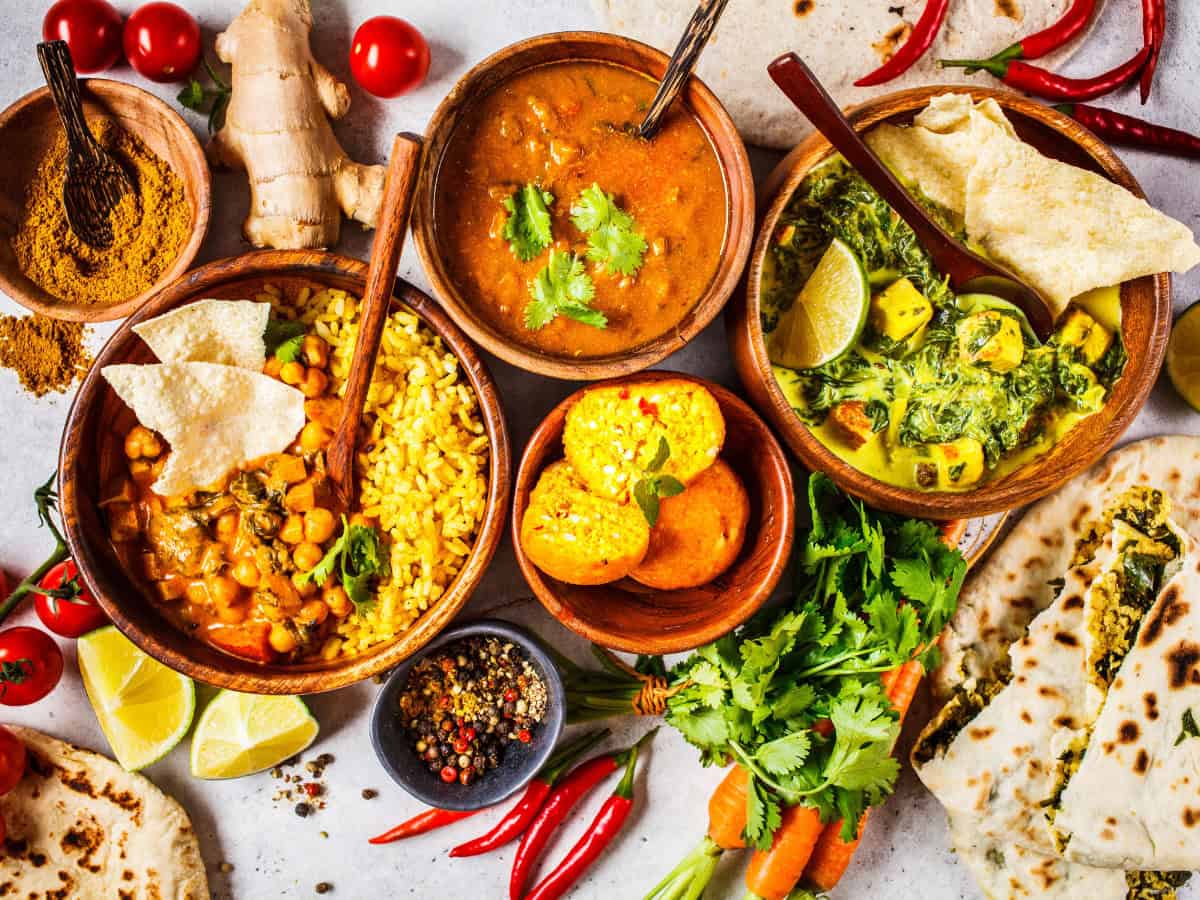 Colorful spread of accidentally vegan Indian foods, including chickpea curry, spinach curry, yellow rice, papad, naan, and traditional Indian sides.