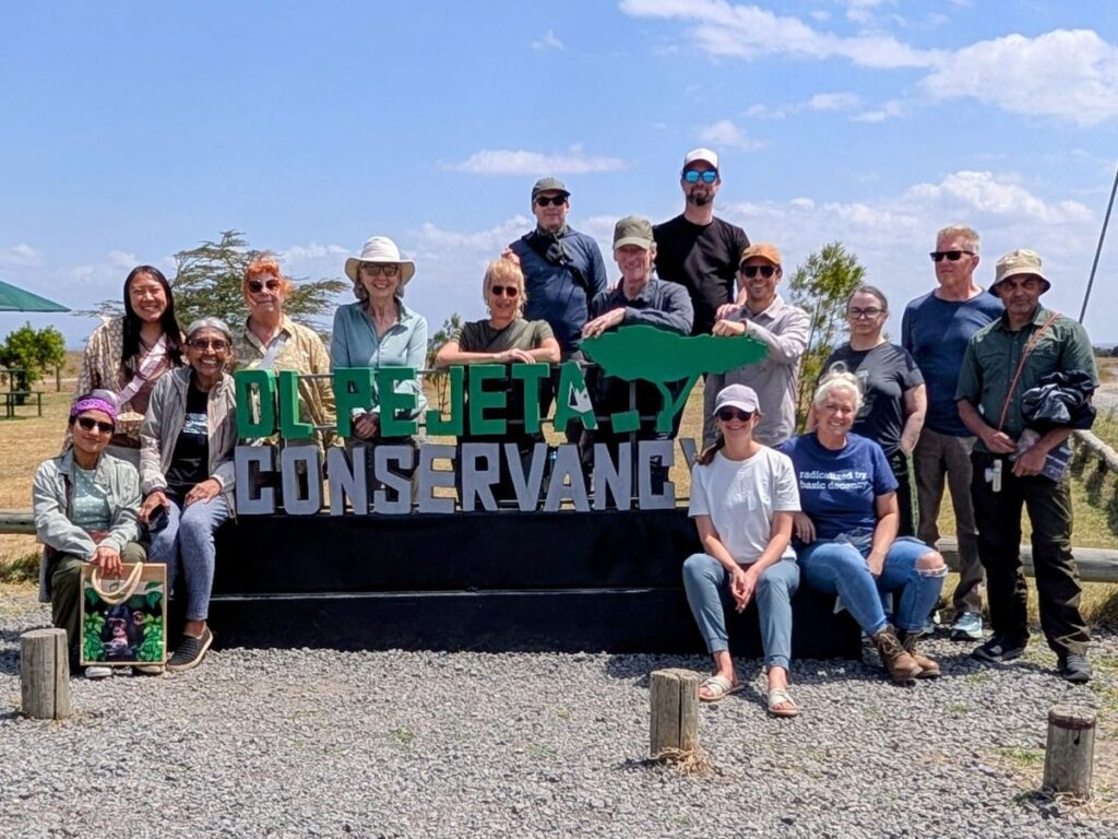 group of travelers sitting and standing around the OI Pejeta sign before starting a vegan safari with veggies abroad