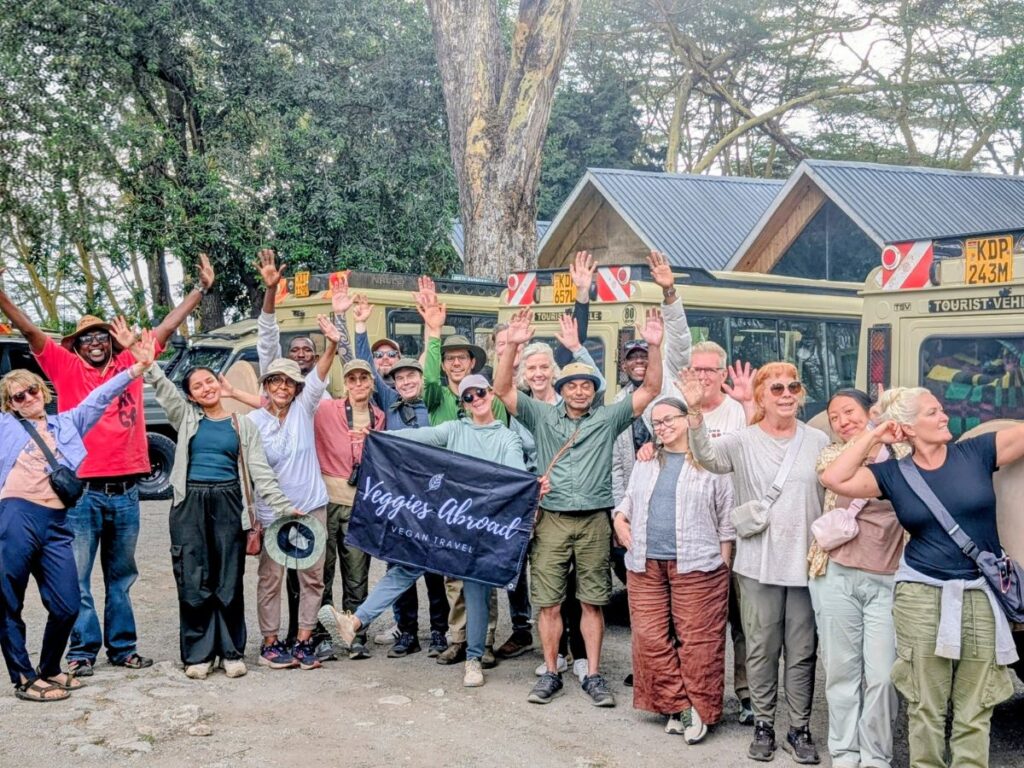 large group of happy vegan travelers posing in front of safari jeeps at the end of a vegan safari through kenya with veggies abroad