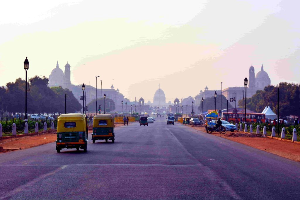 Auto rickshaws driving along Rajpath toward Rashtrapati Bhavan in New Delhi, India, with historic government buildings lining the boulevard.