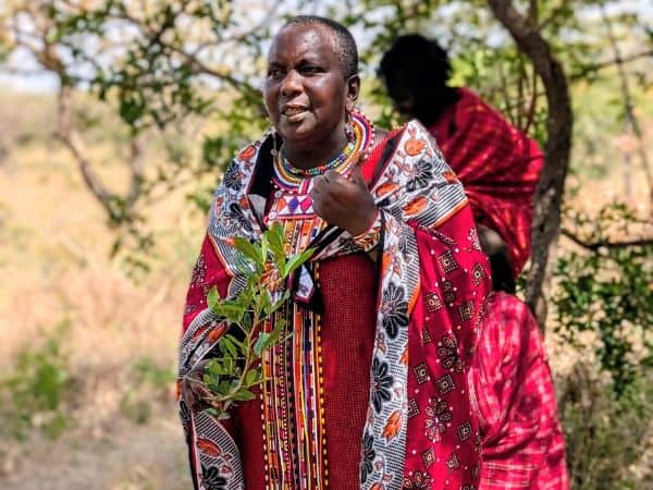 a maasai woman wearing traditional red clothing talking to a group of travelers