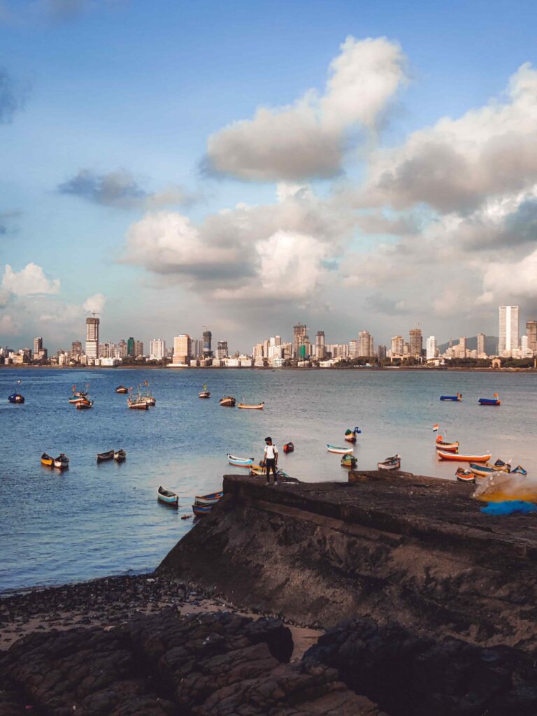 View of Mumbai's waterfront skyline with colorful fishing boats anchored along the Arabian Sea at sunset.