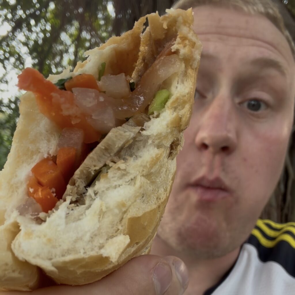Josh enjoying a vegan banh mi sandwich filled with fresh vegetables in Hanoi, Vietnam.