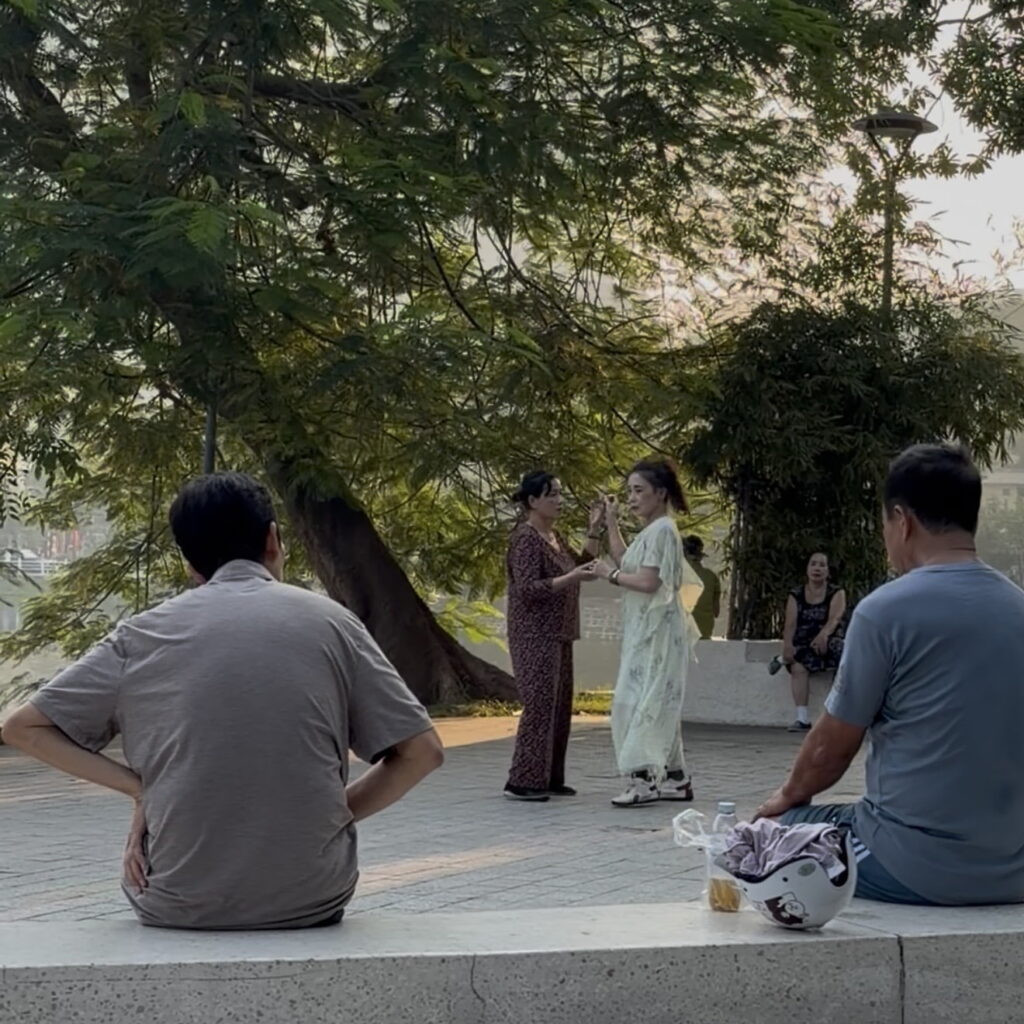 Locals dancing together outdoors near a lake in Hanoi, Vietnam.