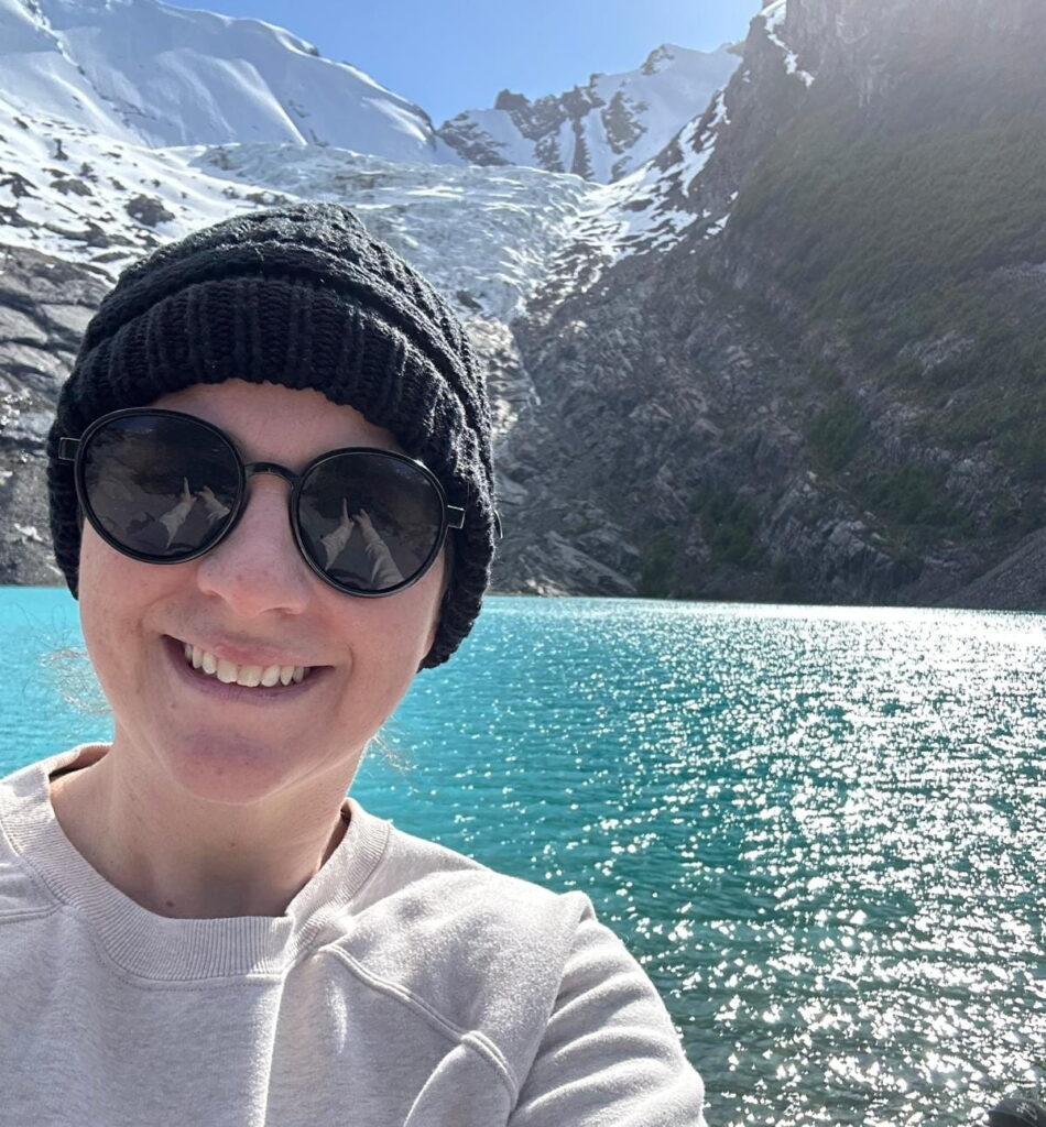 Tatiana Mendolicchio in front of a cold turquoise lake with snowy mountains in the back
