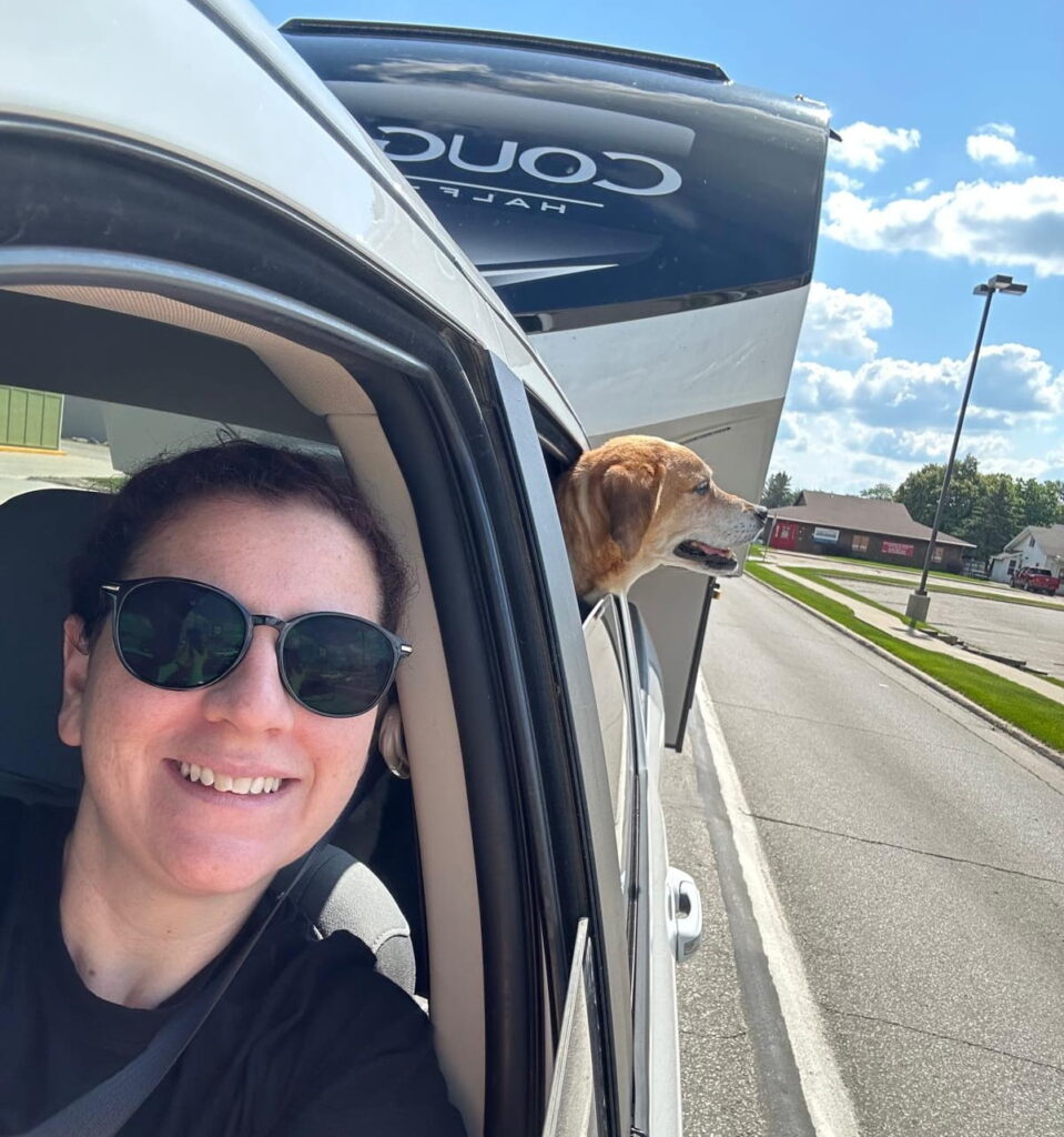 Tatiana driving a truck with a camper with a dog hanging his head out the window