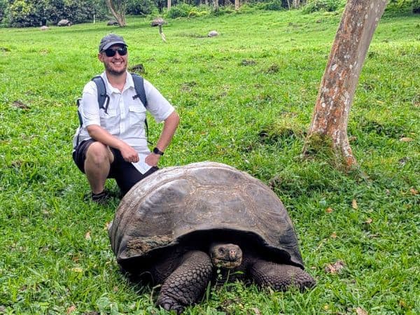 a veggies abroad traveler standing behind a massive tortoise in the galapagos